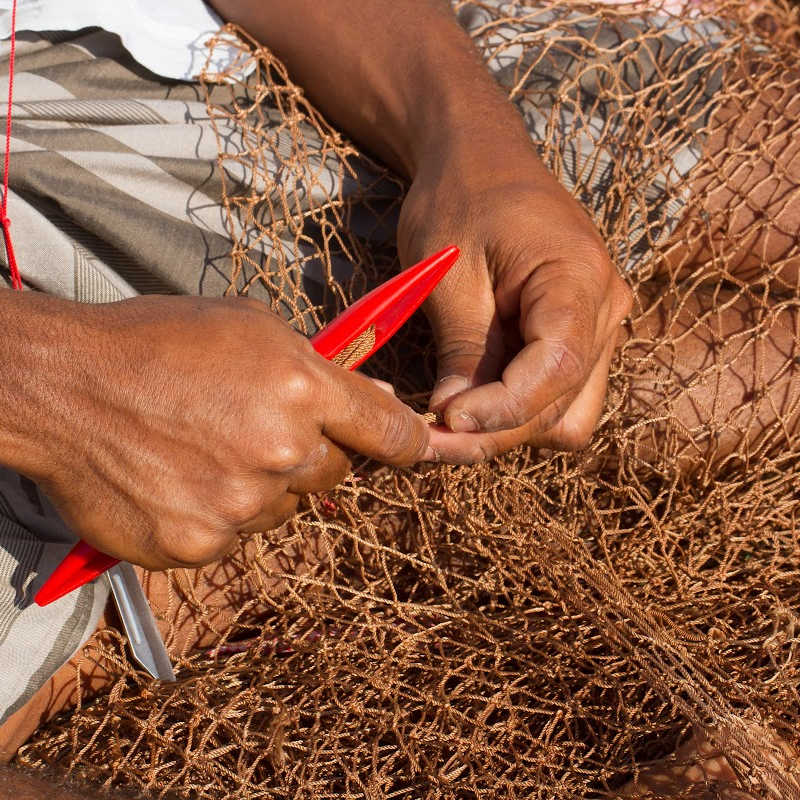Close-up of hands repairing or weaving a fishing net with a red netting shuttle.