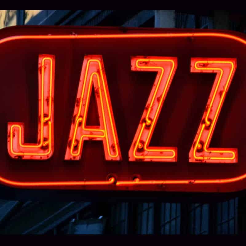 Neon sign glowing bright red with the word “JAZZ” against a dark background, symbolizing live music or a jazz club atmosphere.