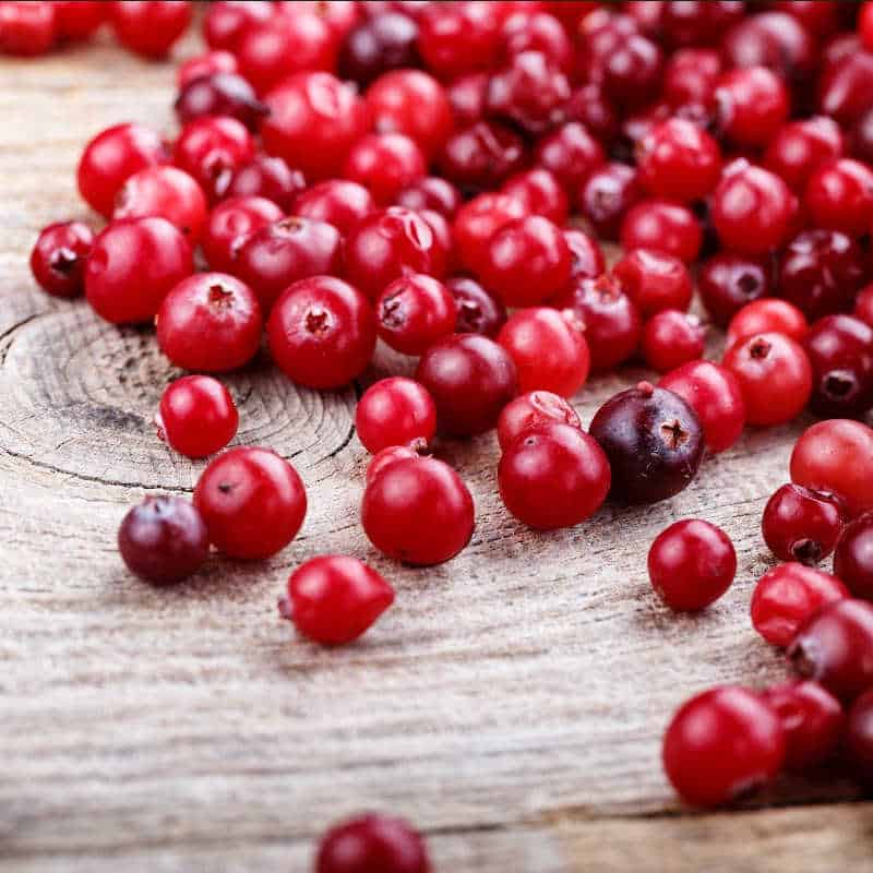 Fresh red cranberries scattered across a wooden surface, representing seasonal harvest and local foodways.