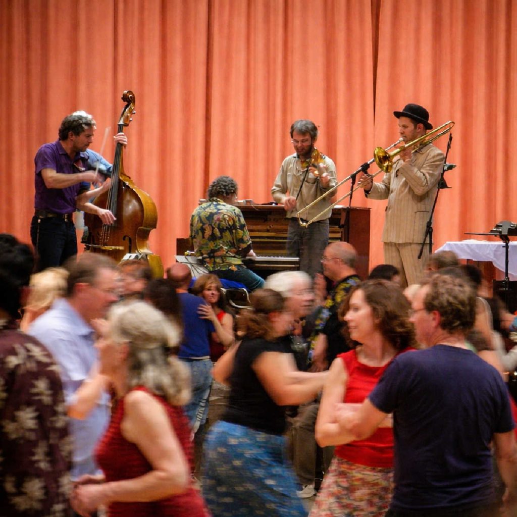 Contra Dancing: Live band plays on stage while dancers move together during a lively contra dance.