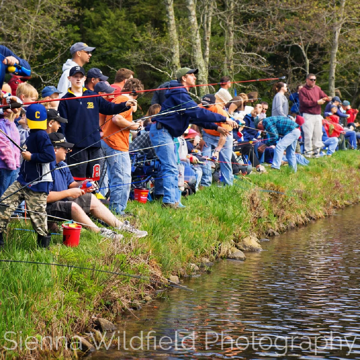 Fishing Derby: Adults and children line the edge of a pond with fishing rods during a group fishing event, emphasizing outdoor recreation and intergenerational learning.