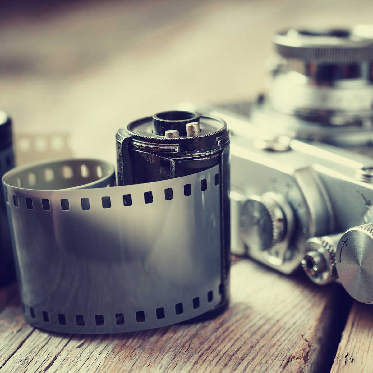A close-up of a vintage camera with an exposed film canister and a strip of photographic film resting on a wooden surface.