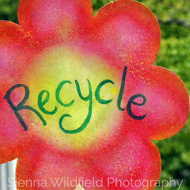 Hand-painted flower-shaped sign with the word “Recycle” written in green letters.